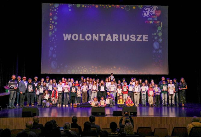 grupa wolontariuszy Wielkiej Orkiestry Świątecznej Pomocy na scenie sali widowiskowej 