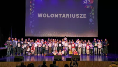 grupa wolontariuszy Wielkiej Orkiestry Świątecznej Pomocy na scenie sali widowiskowej 